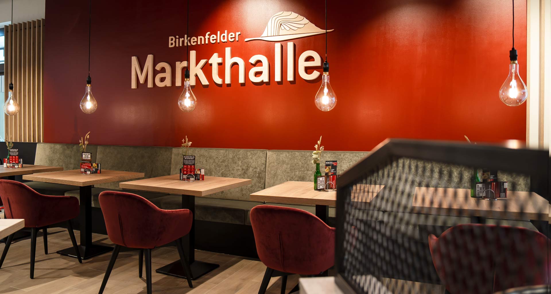 Innenraum der Birkenfelder Markthalle mit roten Samtstühlen, Hängelampen und dekorierten Tischen
